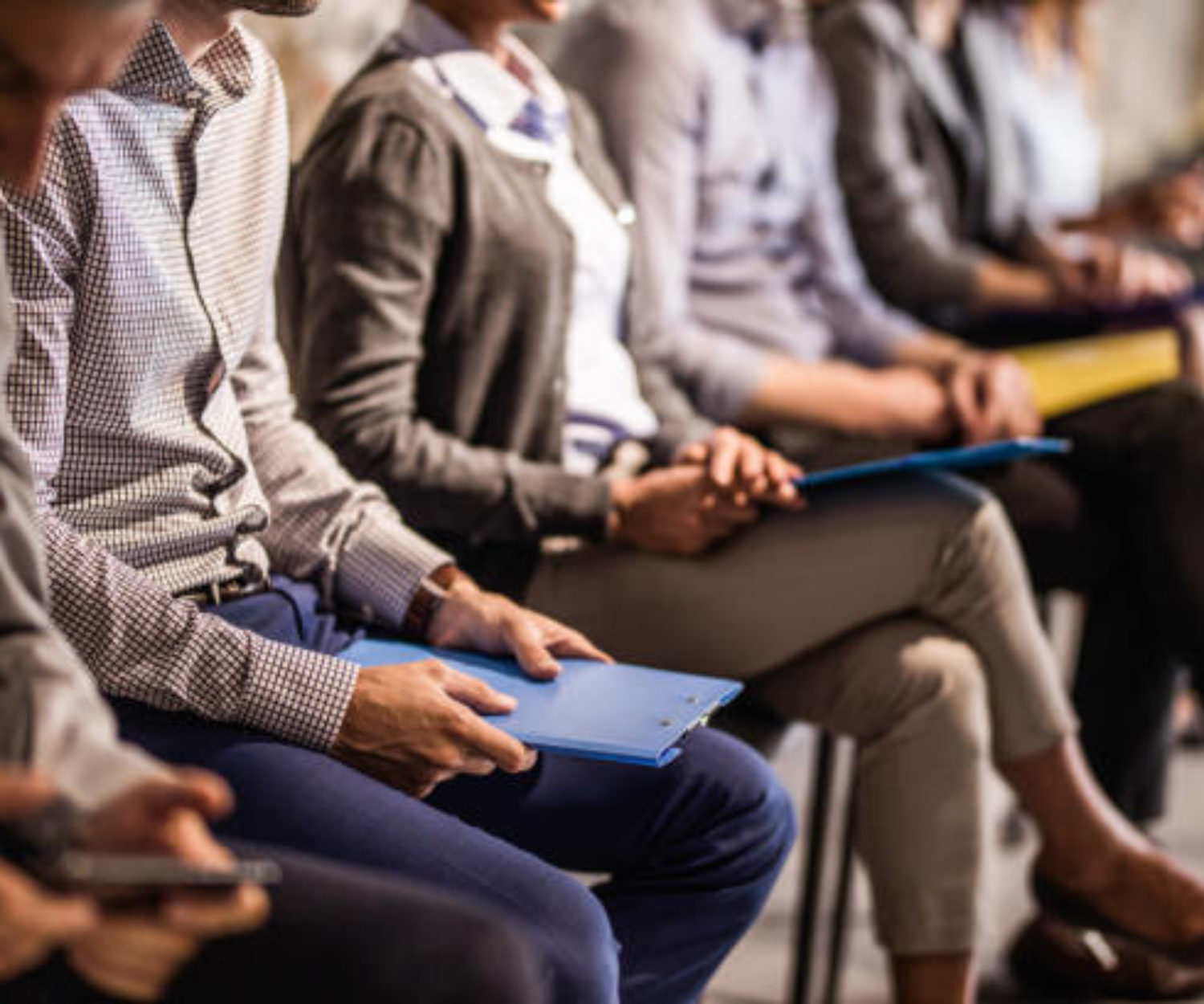 Large group of unrecognizable business people waiting for a job interview. Focus is on man with blue clipboard.